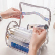 Mani che aprono una borsa trasparente per cosmetici con flaconi di profumo e lozioni. Organizzatore da viaggio, accessori beauty, pratico e elegante.