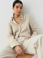 Donna con camicia beige in lino, seduta su sedia. Moda casual elegante, abbigliamento donna, stile minimalista. Sfondo bianco.