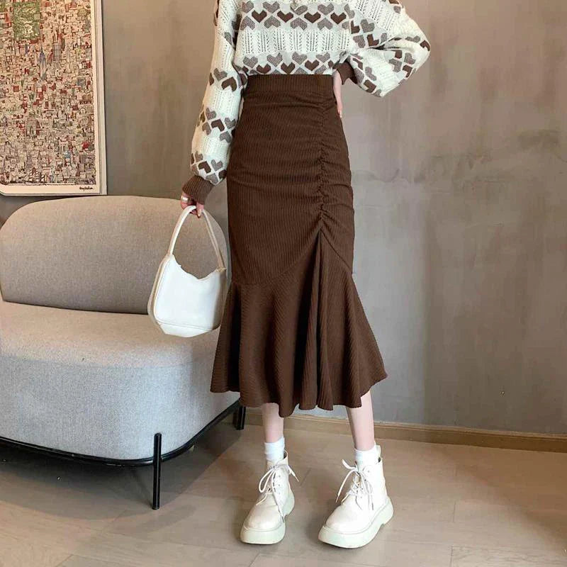 Donna con maglione a cuori e gonna marrone a pieghe, borsa bianca e stivali alti. Moda autunnale, abbigliamento casual chic.