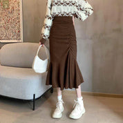 Donna con maglione a cuori e gonna marrone a pieghe, borsa bianca e stivali alti. Moda autunnale, abbigliamento casual chic.