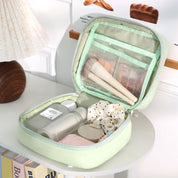 Astuccio da viaggio verde aperto con pennelli trucco, flaconi cosmetici e accessori su tavolo bianco. Organizzatore cosmetici compatto ed elegante.