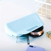 Astuccio cosmetico azzurro in pelle sintetica con cerniera, contenente trucco e pennello. Design elegante, ideale per organizzare prodotti di bellezza.