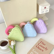 Tre borse a forma di triangolo in colori pastello (verde, blu, viola) su un tavolo con una tazza di tè, un tulipano e un libro. Design moderno e colorato.