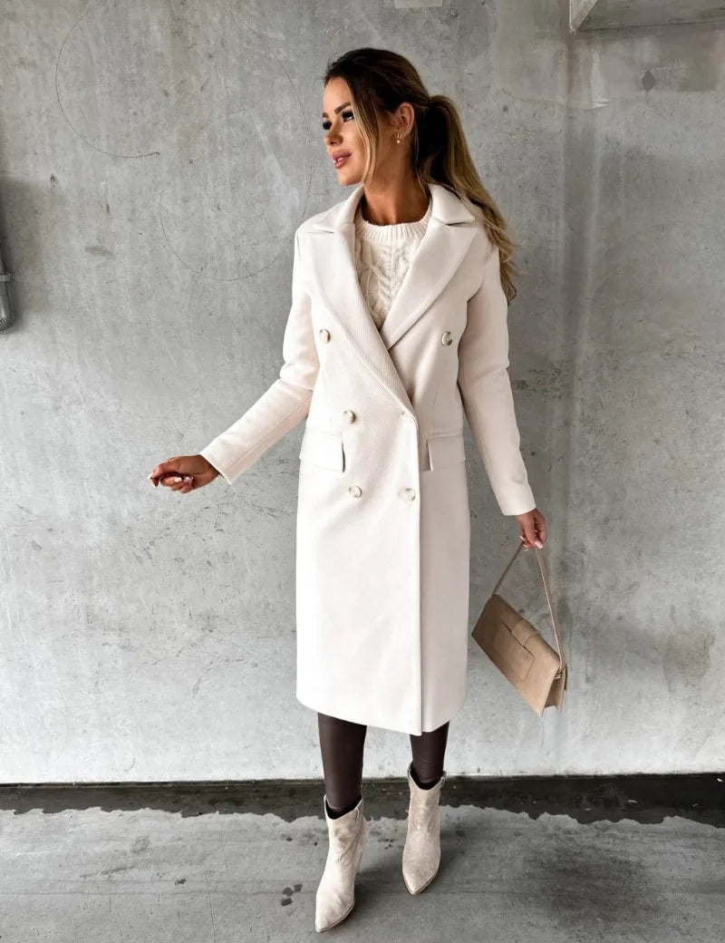 Donna con cappotto bianco elegante, borsa beige e stivali chiari, posa su sfondo grigio. Moda autunnale, stile chic, abbigliamento femminile.