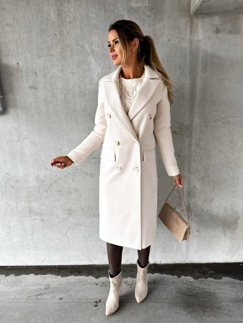 Donna con cappotto bianco elegante, borsa beige e stivali chiari, posa su sfondo grigio. Moda autunnale, stile chic, abbigliamento femminile.