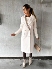 Donna con cappotto bianco elegante, borsa beige e stivali chiari, posa su sfondo grigio. Moda autunnale, stile chic, abbigliamento femminile.
