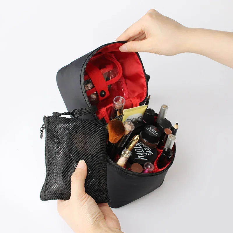 Borsa trucco nera aperta con interno rosso, contenente vari cosmetici e pennelli, accanto a una pochette a rete nera. Accessori make-up organizzati.