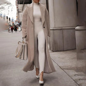 Donna elegante in cappotto beige e abito bianco, cammina in città con borsa coordinata. Moda autunnale, stile urbano chic, abbigliamento femminile.