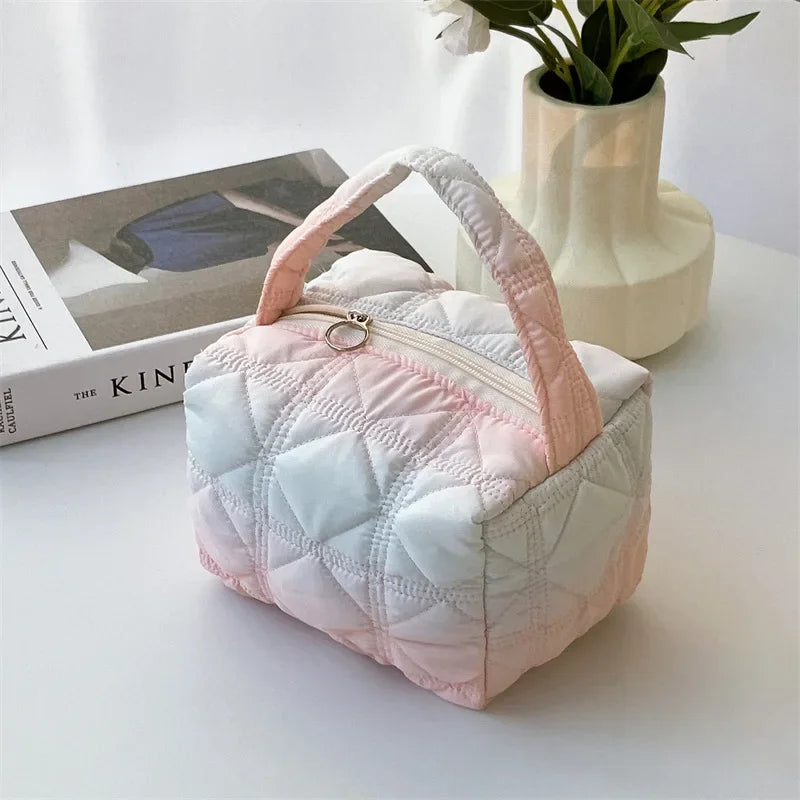 Borsa cosmetica trapuntata rosa e bianca su tavolo bianco, con libro e vaso di fiori. Design elegante, ideale per viaggi e organizzazione trucco.