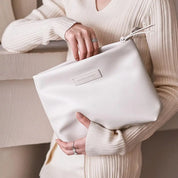 Donna con maglione beige tiene una borsa clutch bianca in pelle, elegante e minimalista, ideale per moda autunnale. Accessorio di tendenza.