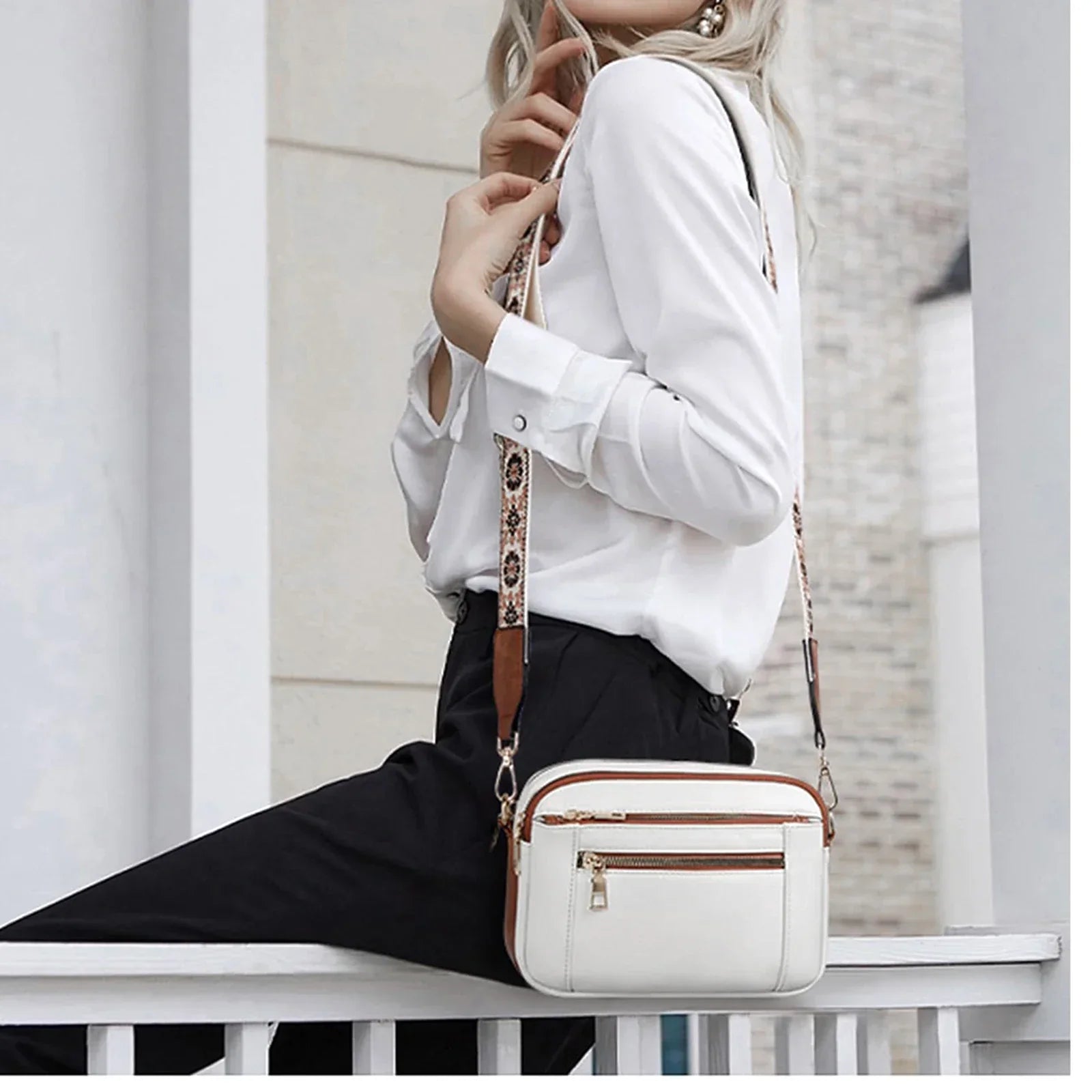 Donna con borsa a tracolla bianca in pelle, dettagli marroni, indossa camicia bianca e pantaloni neri. Moda elegante, accessori femminili.