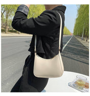 Donna con borsa a tracolla beige su strada alberata. Moda femminile, accessori eleganti, stile casual chic. Perfetta per shopping e uscite quotidiane.