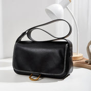 Borsa a tracolla in pelle nera su tavolo bianco, design elegante con cuciture a contrasto, lampada moderna sullo sfondo. Accessorio moda donna.
