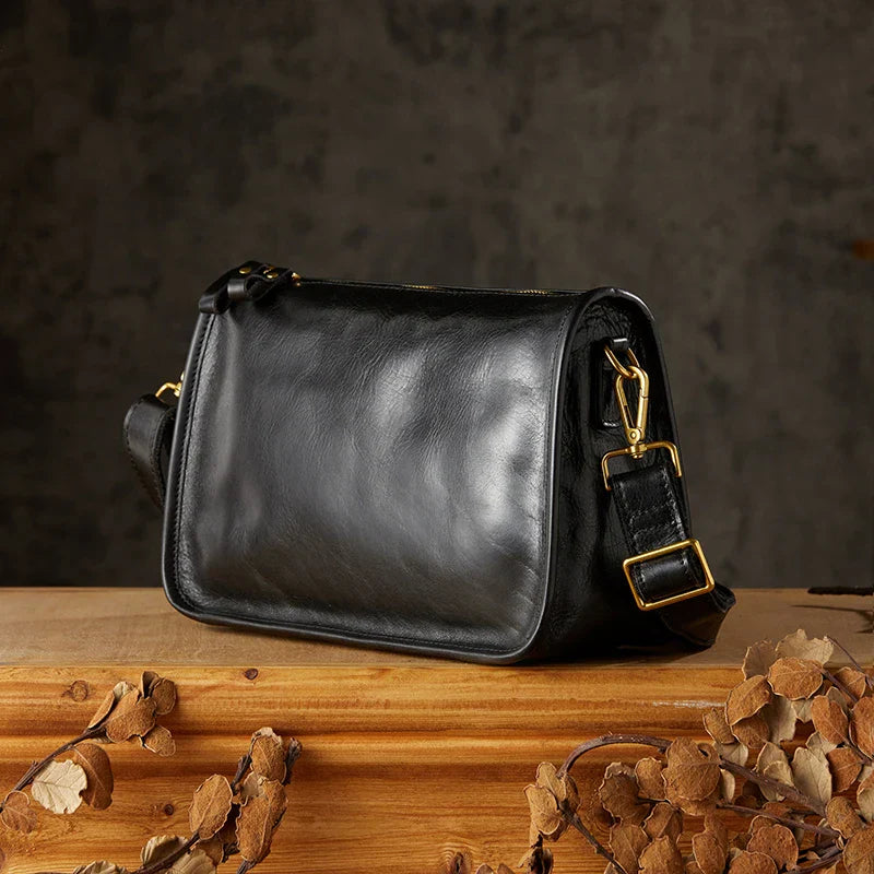 Borsa a tracolla in pelle nera su tavolo di legno, design elegante con fibbie dorate. Accessorio moda donna, stile classico e raffinato.