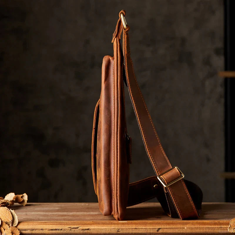 Borsa a tracolla in pelle marrone su tavolo di legno, design elegante e sottile, ideale per uomo, accessorio moda, stile vintage.