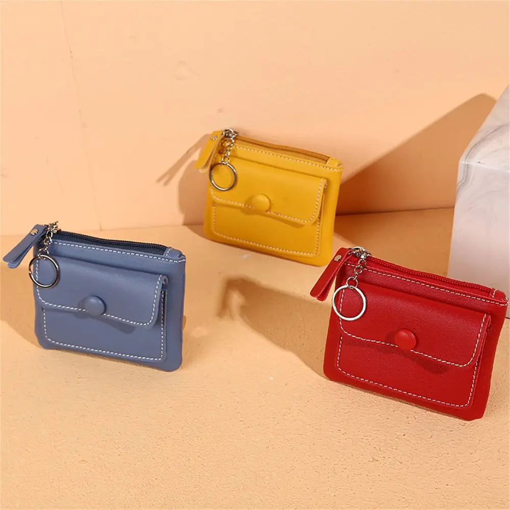 Tre portamonete in pelle colorata con cerniera e anello portachiavi, nei colori blu, giallo e rosso, su sfondo beige. Accessori moda eleganti.