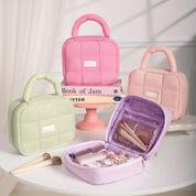 Quattro borse cosmetiche imbottite in colori pastello su tavolo bianco, con accessori trucco. Ideali per organizzare e trasportare prodotti di bellezza.