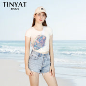 Giovane donna in spiaggia con marsupio olografico TINYAT, cappellino bianco e shorts di jeans. Accessorio moda estivo, stile casual.