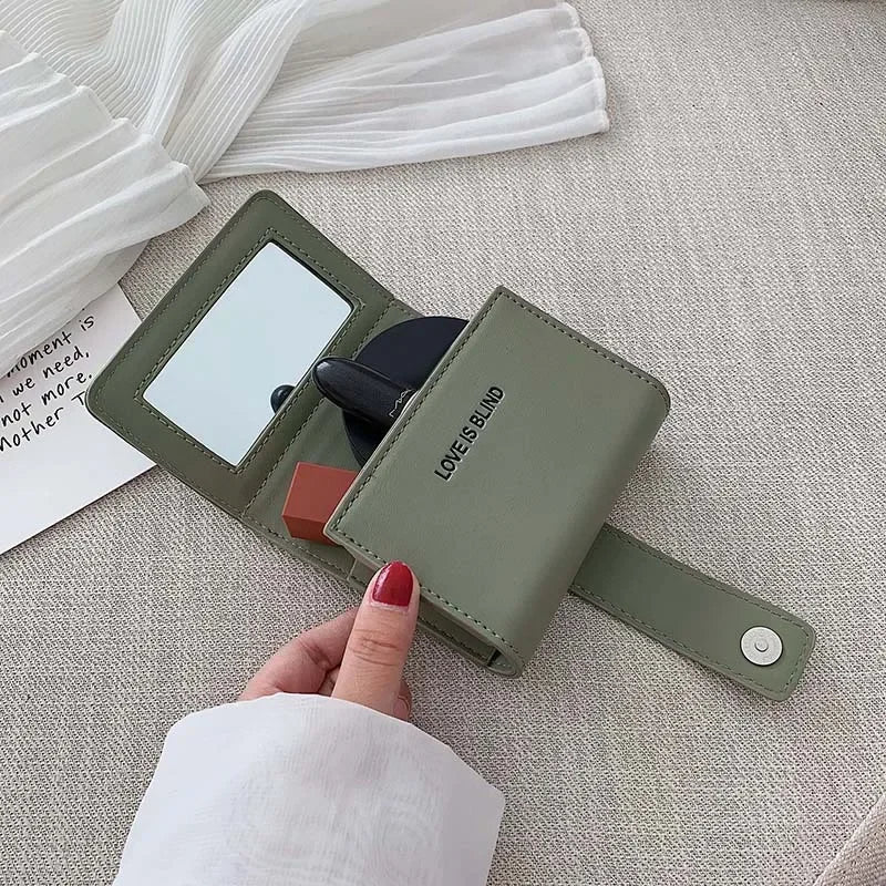 Portafoglio verde in pelle con specchio integrato, chiusura a bottone, design compatto. Accessorio moda elegante per donna.
