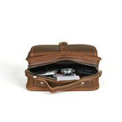 Borsa a tracolla in pelle marrone aperta, con zip, contenente oggetti personali. Design elegante, ideale per uomo e donna. Accessorio moda versatile.