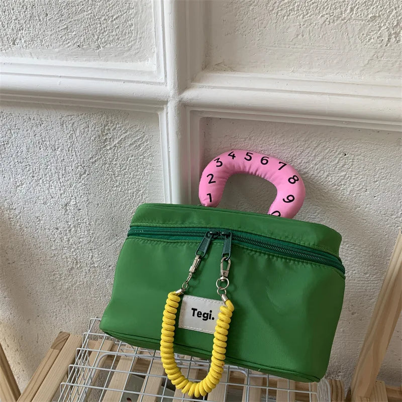 Borsa verde con manico rosa numerato, design moderno, chiusura a zip, decorazione gialla, su sfondo bianco. Accessorio moda unico e colorato.