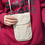 Borsa a tracolla beige unisex, indossata su felpa rossa. Design compatto, ideale per viaggi e uso quotidiano. Tasche multiple, stile casual.
