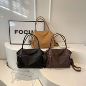 Tre borse a mano eleganti in pelle nera, marrone e beige su un tavolo bianco, con un quadro con la scritta "FOCUS" sullo sfondo.