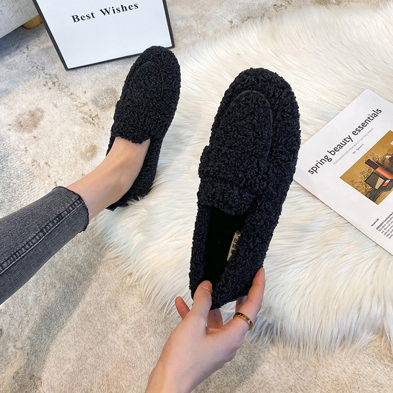 Scarpe mocassini donna in pelliccia sintetica nera, su tappeto bianco. Design elegante e confortevole, perfette per l'autunno e l'inverno.