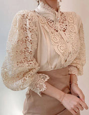 Blusa elegante in pizzo beige con maniche a sbuffo, dettagli floreali e colletto alto. Moda femminile, abbigliamento chic, stile vintage.