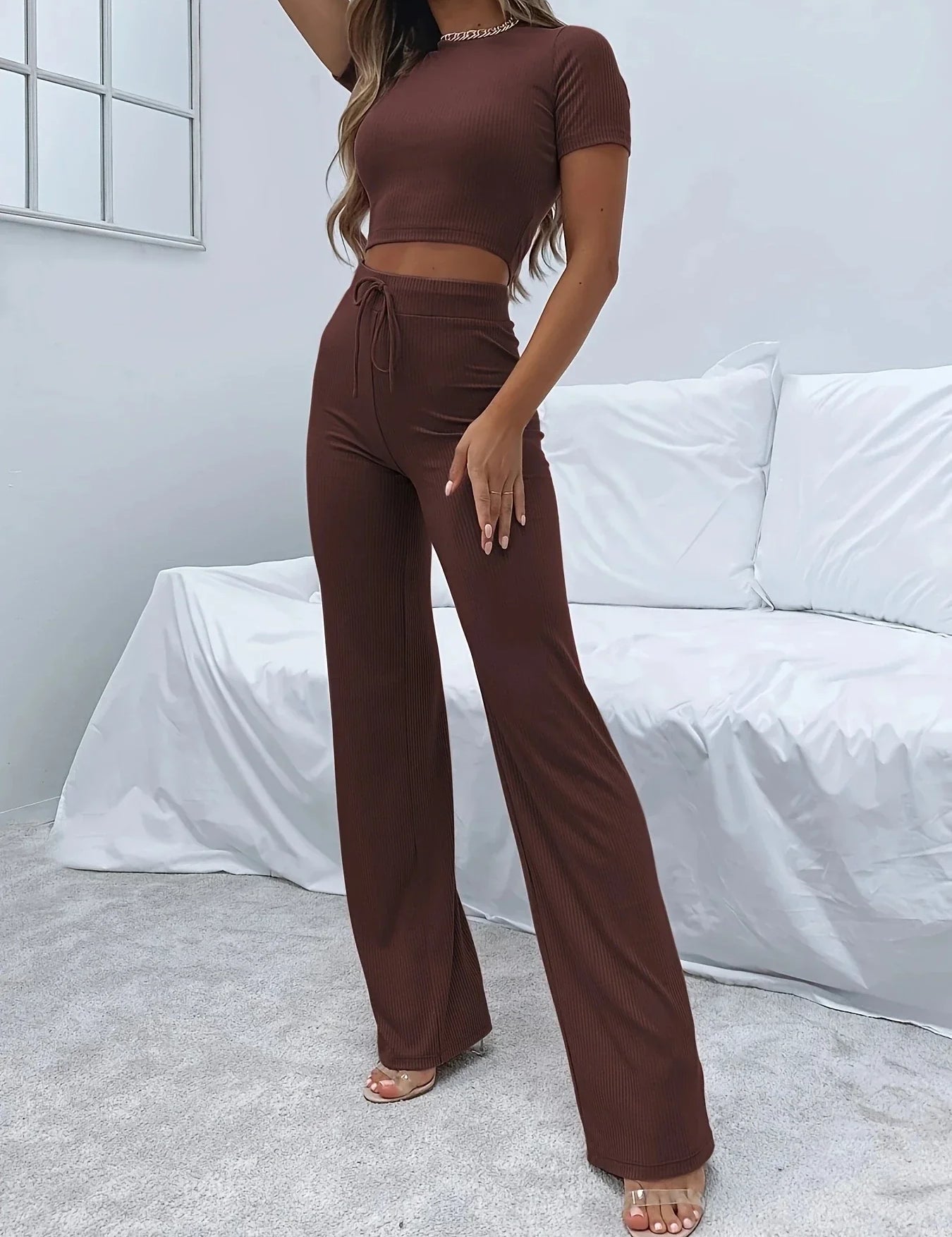 Donna in completo marrone a coste, top corto e pantaloni a zampa, in salotto moderno. Abbigliamento casual elegante, moda femminile autunnale.