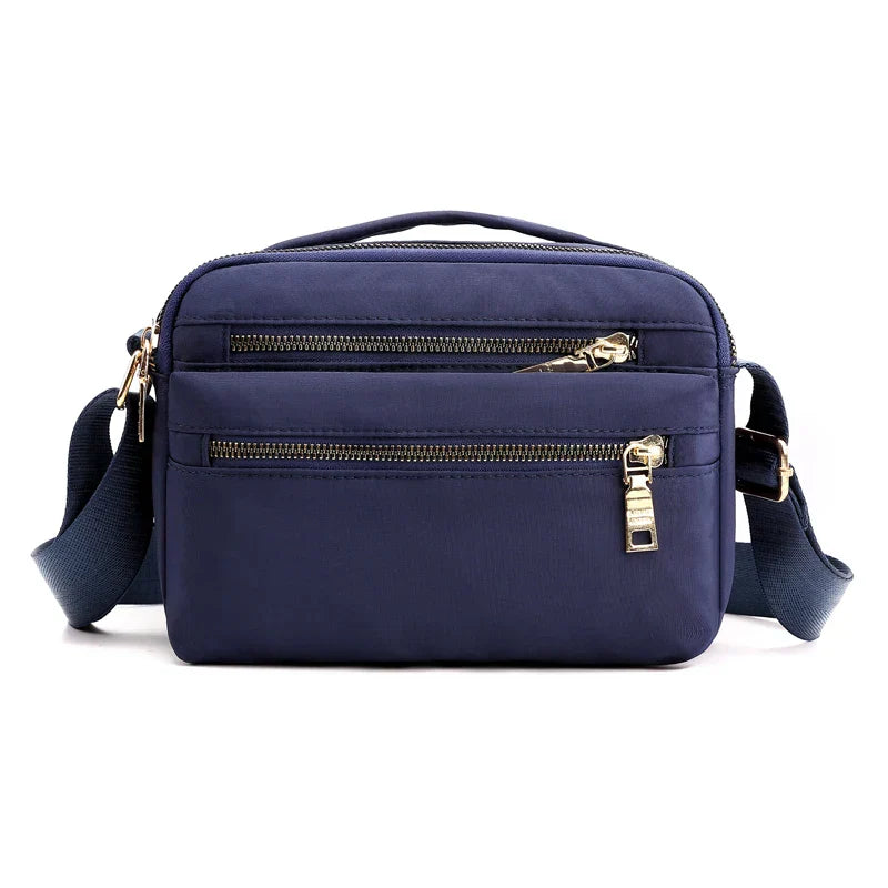 Borsa a tracolla blu in nylon con doppia cerniera, tasche frontali, manico superiore e tracolla regolabile. Accessorio moda pratico ed elegante.