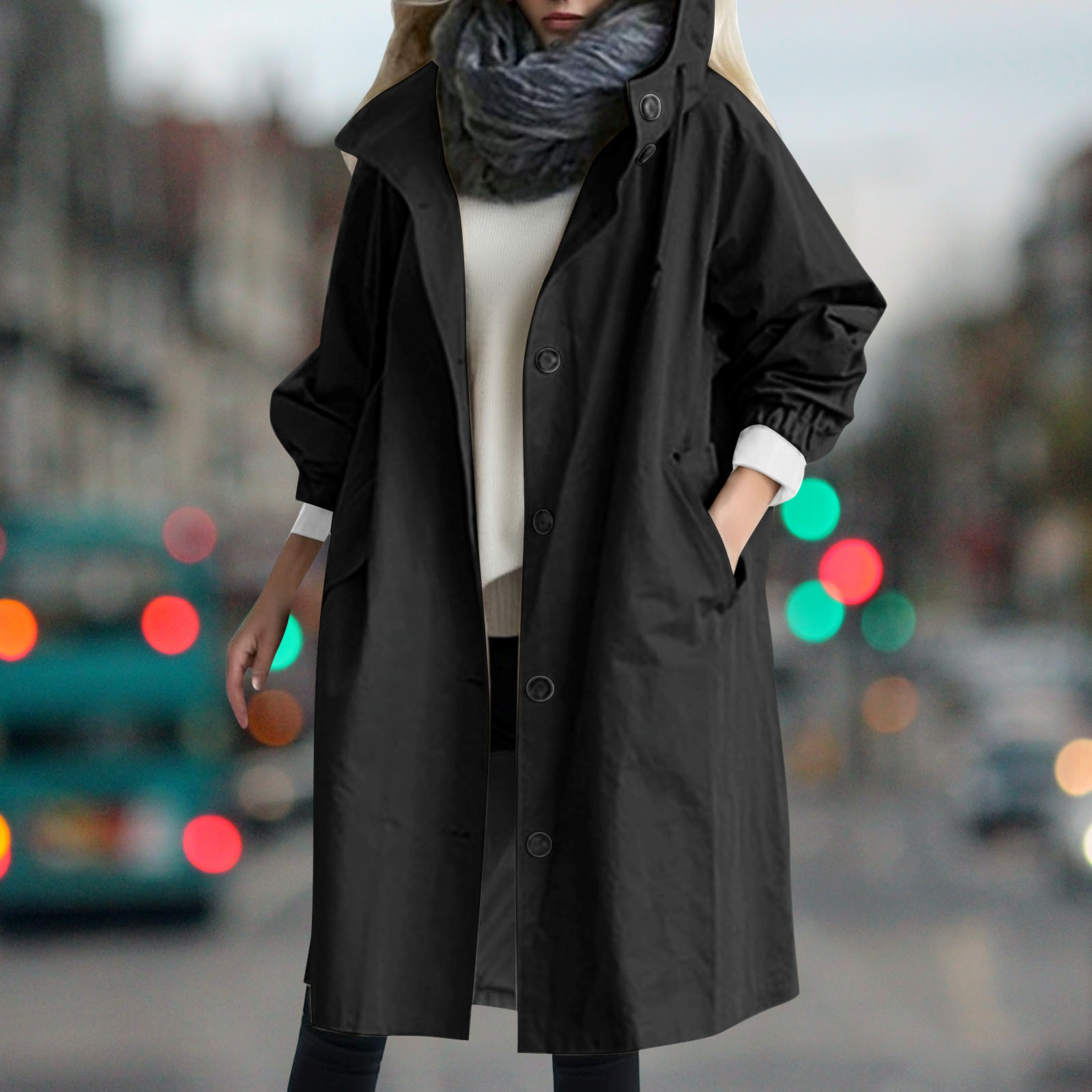 Cappotto nero lungo da donna, elegante e casual, indossato su maglione bianco. Perfetto per l'autunno, moda urbana, sfondo sfocato di città.