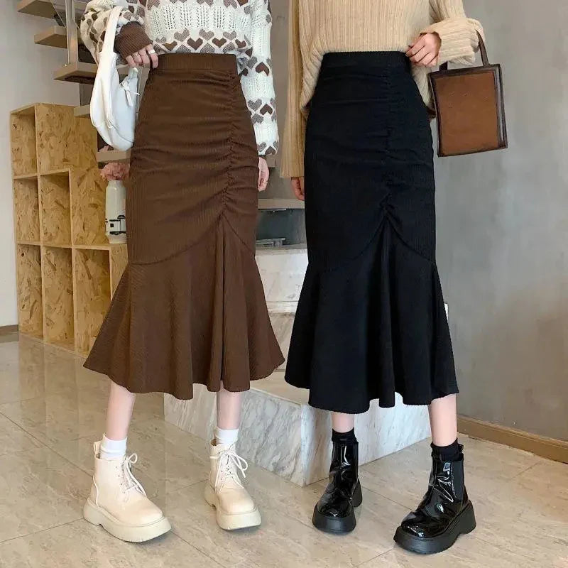 Due donne in gonne midi a sirena, una marrone e una nera, con stivali alla moda. Abbigliamento autunnale elegante e casual.