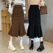 Due donne in gonne midi a sirena, una marrone e una nera, con stivali alla moda. Abbigliamento autunnale elegante e casual.