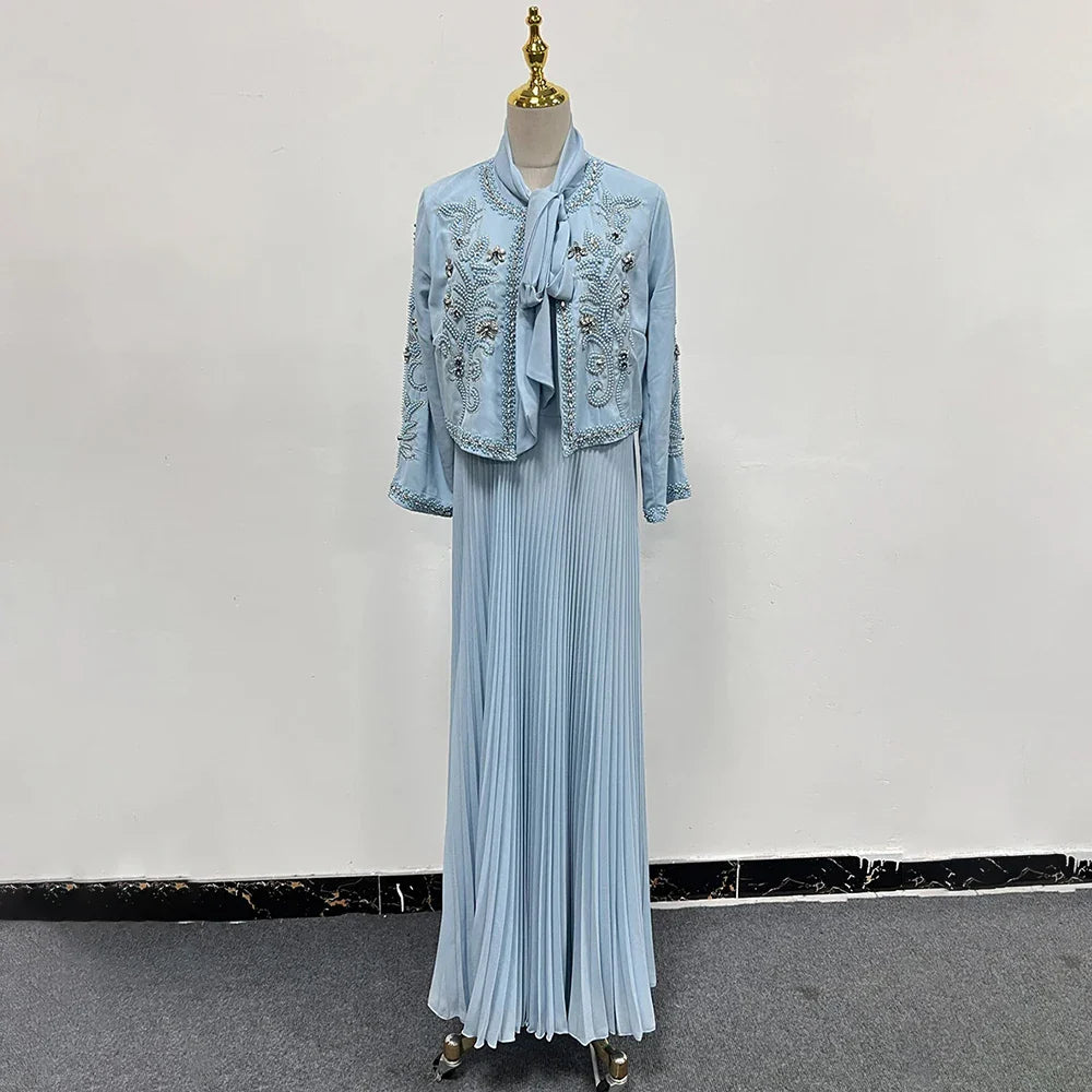 Abito lungo azzurro con giacca ricamata, manichino sartoriale, moda elegante, tessuto plissettato, abbigliamento donna, stile sofisticato.