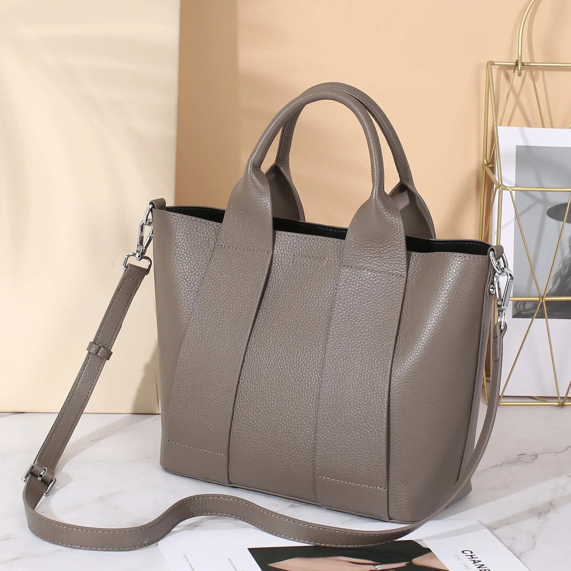 Borsa a mano in pelle grigia con tracolla regolabile, design elegante e moderno, su sfondo neutro. Accessorio moda donna, stile casual chic.