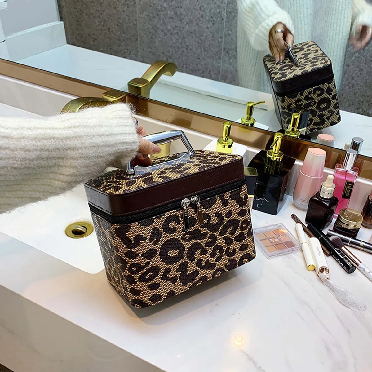 Borsa cosmetica leopardata su lavabo bagno, con cerniera e manico, accanto a trucchi e profumi. Design elegante, accessorio moda essenziale.