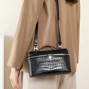 Borsa a tracolla nera in pelle effetto coccodrillo, chiusura con zip e fibbia argentata, indossata su cappotto beige. Accessorio moda elegante.