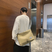 Uomo con maglietta bianca e cappello nero indossa una borsa a tracolla beige in un corridoio moderno. Accessorio moda casual, stile urbano.