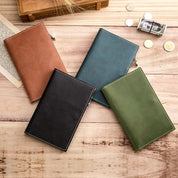 Quattro quaderni in pelle di diversi colori (marrone, verde, nero, blu) su tavolo di legno, con monete e banconote. Accessori eleganti per ufficio.