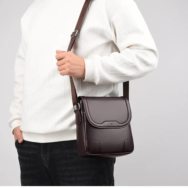 Borsa a tracolla in pelle marrone scuro per uomo, indossata su maglione bianco e jeans neri. Accessorio elegante e pratico per uso quotidiano.