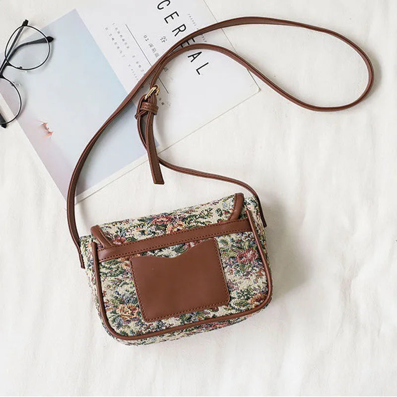 Borsa a tracolla floreale vintage con dettagli in pelle marrone, occhiali e rivista su sfondo bianco. Accessorio moda donna elegante e retrò.