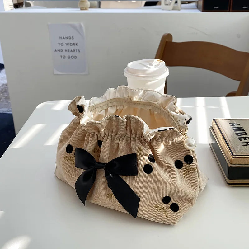 Borsa in tessuto beige con fiocco nero e decorazioni a pois, su tavolo bianco accanto a tazza di caffè e scatola. Accessorio moda elegante.
