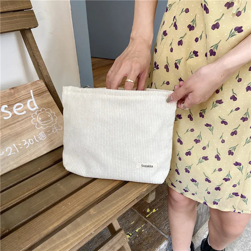 Donna con abito giallo a fiori tiene una borsa a tracolla bianca in tessuto a coste. Accessorio moda estivo, stile casual chic.