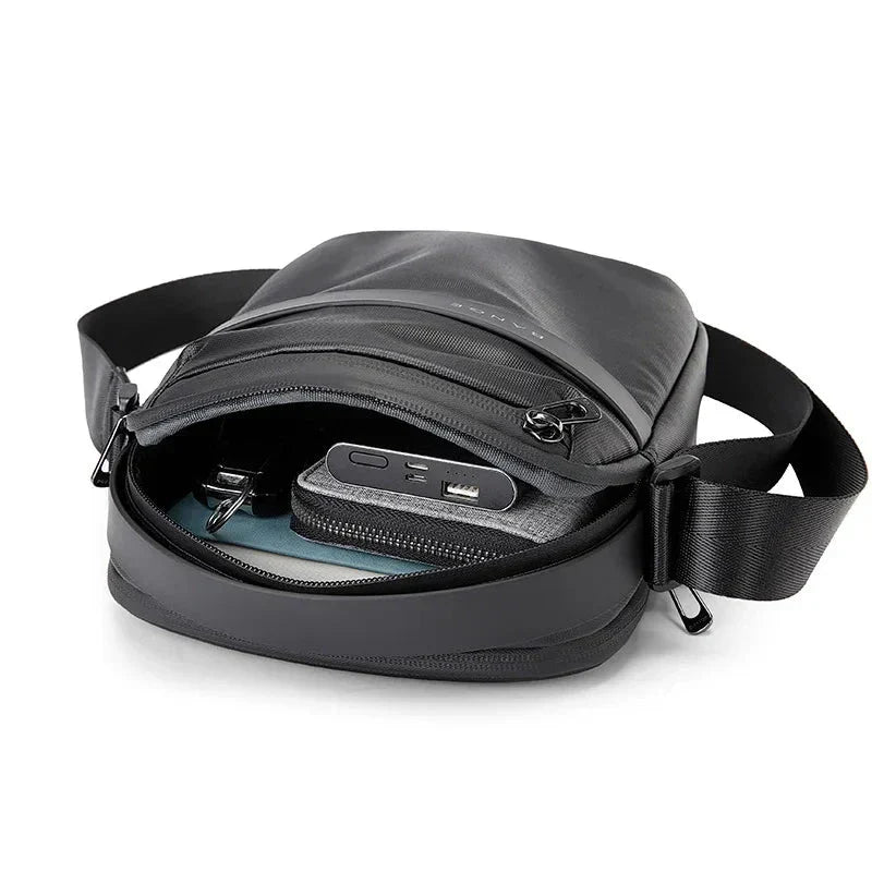 Zaino a tracolla nero in pelle, con scomparto aperto che mostra power bank, cavi e tablet. Design moderno, ideale per viaggi e lavoro.