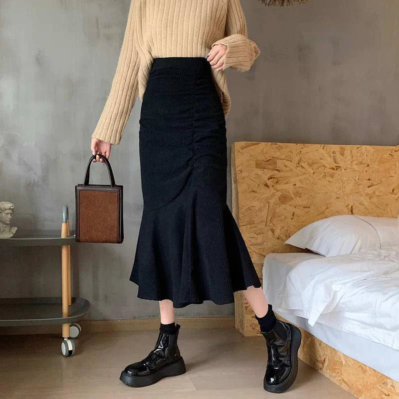 Donna con maglione beige e gonna nera a vita alta, scarpe nere lucide, borsa marrone. Moda autunnale elegante, outfit casual chic.