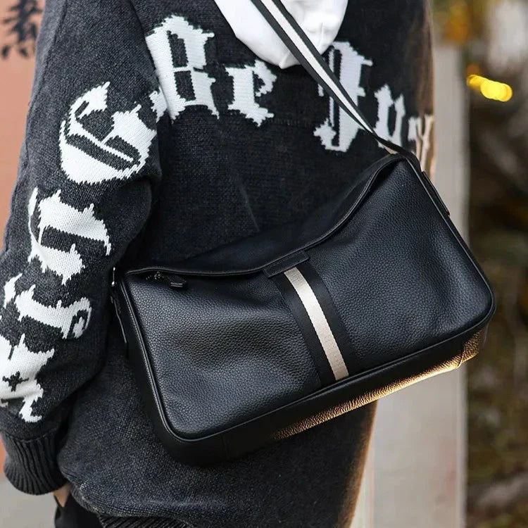Borsa a tracolla in pelle nera con striscia centrale grigia, indossata su felpa con cappuccio. Accessorio moda uomo, stile casual ed elegante.