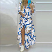 Abito lungo donna con stampa a catene blu e oro, maniche lunghe, scollo a V, spacchi frontali, indossato con sneakers bianche. Moda elegante casual.