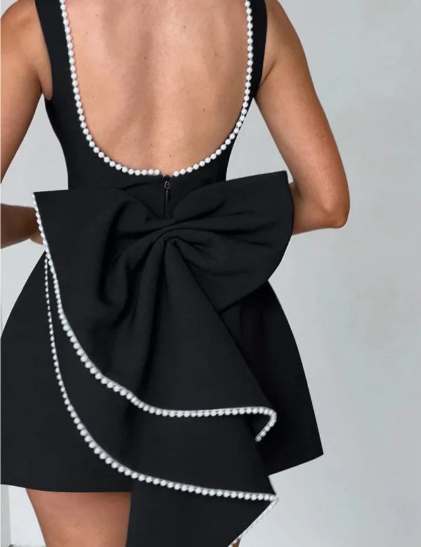 Abito nero elegante con schiena scoperta, fiocco grande e bordi decorati con perle bianche. Perfetto per eventi serali e cerimonie.