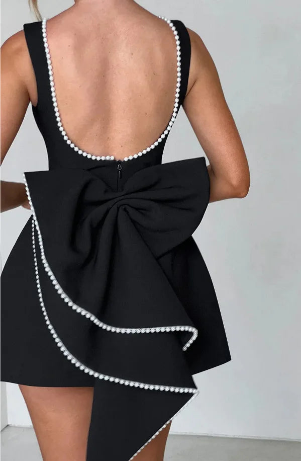Abito nero elegante con schiena scoperta, fiocco grande e bordi decorati con perle bianche. Perfetto per eventi serali e cerimonie.